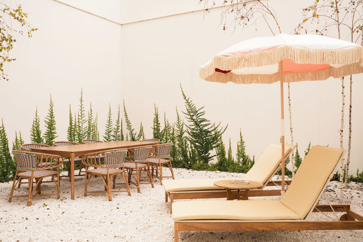 A patio with a wooden table and chairs, a lounge chair, and an umbrella.