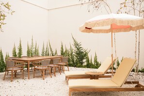 A patio with a wooden table and chairs, a lounge chair, and an umbrella. - The Verse (Lisbon)