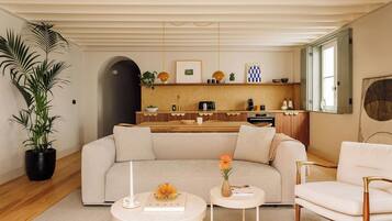 Una sala moderna con sofá, mesa de centro y sillón, además de una cocina con encimera de madera y una planta grande en maceta.