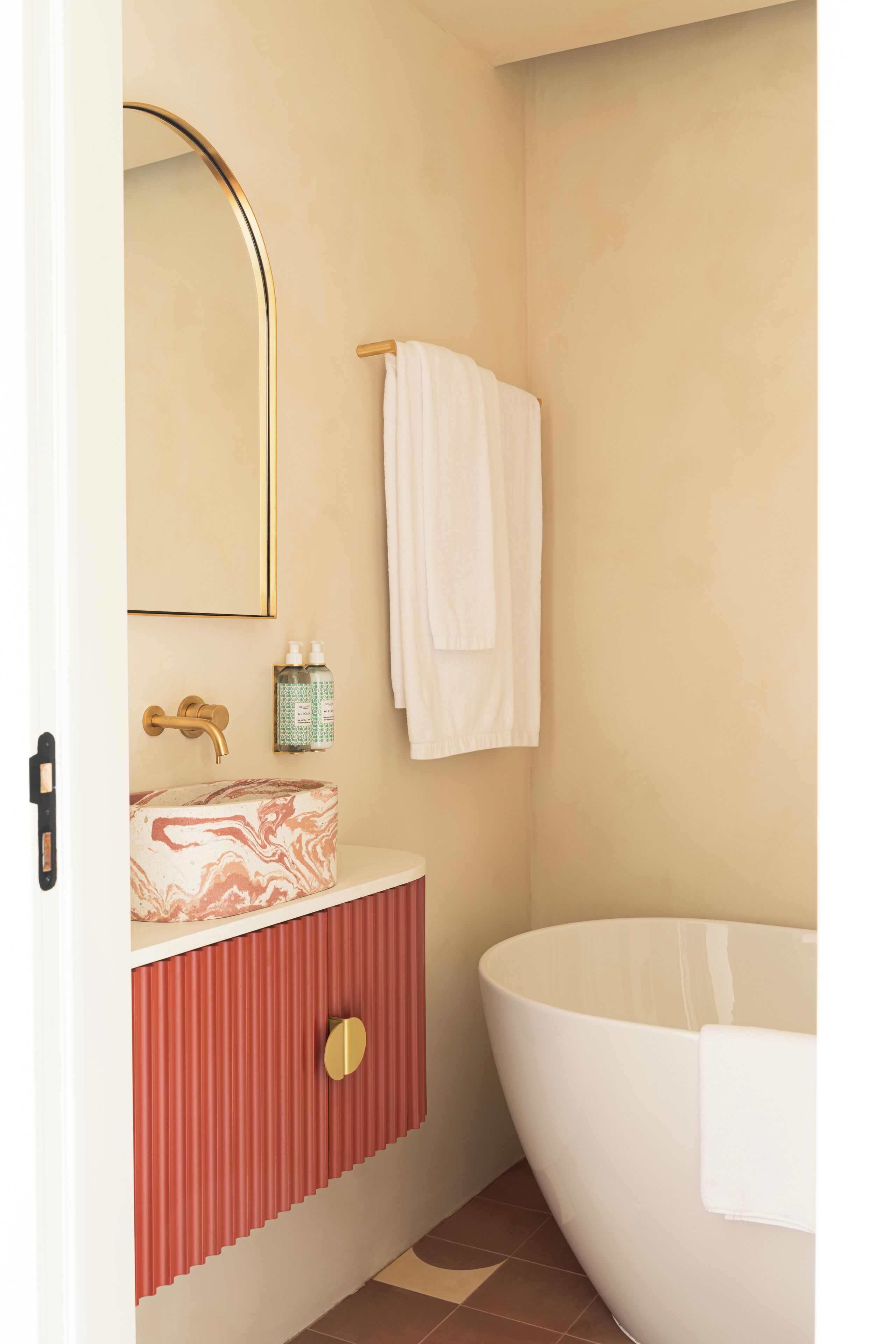 Un baño con lavamanos de mármol, grifo dorado, espejo, toallero y bañera.