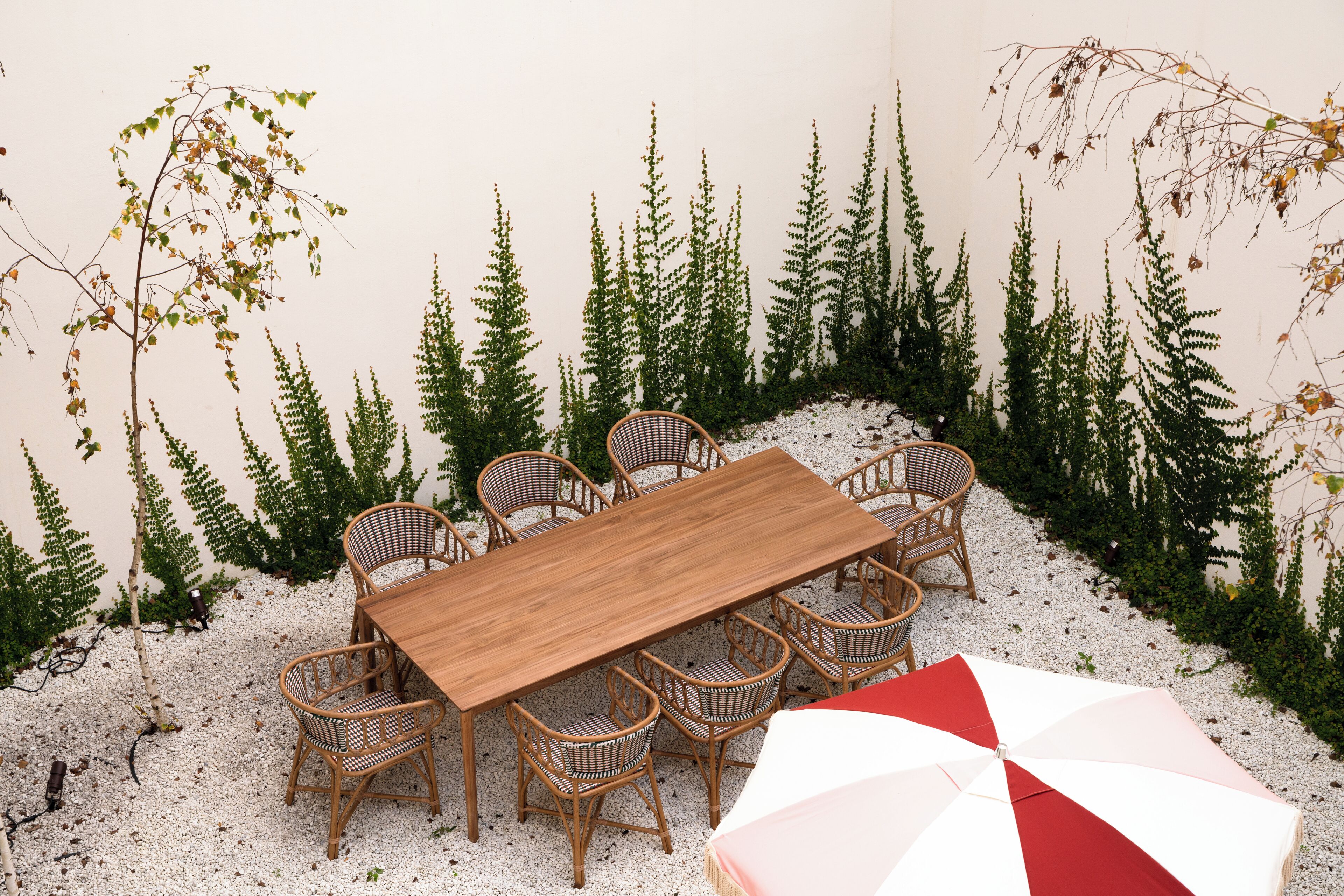 A dining area with a wooden table and wicker chairs, surrounded by artificial greenery.