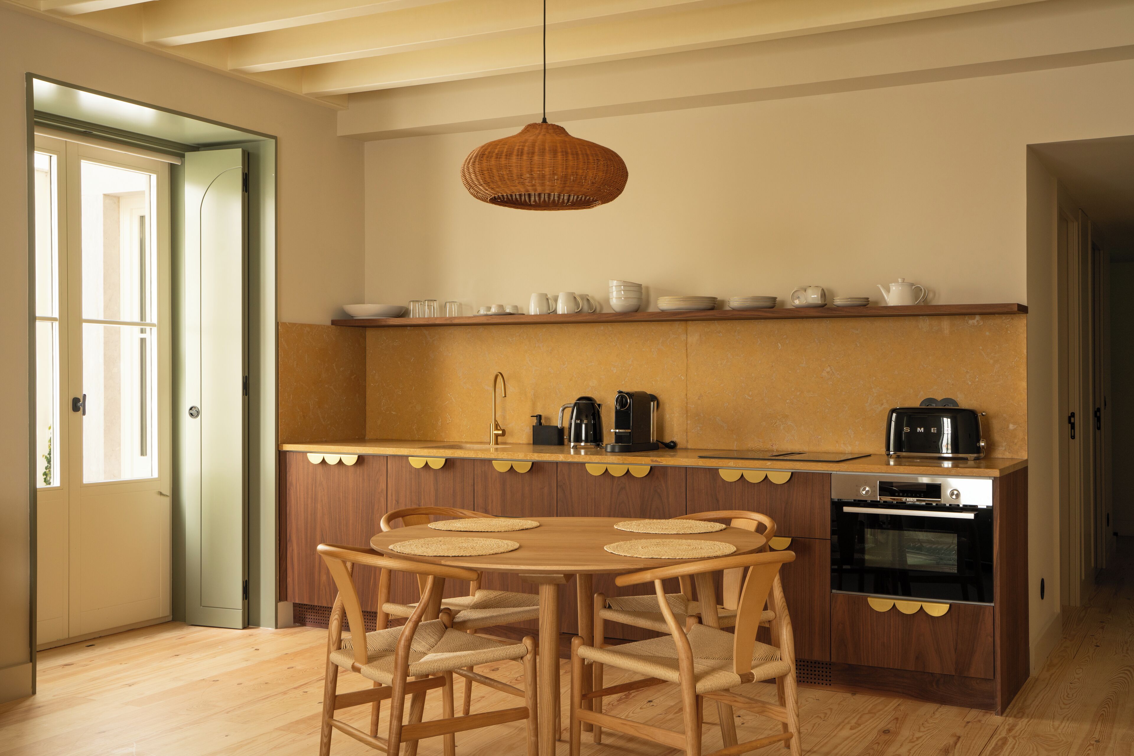 A kitchen with a wooden table, chairs, a hanging light, and a countertop with kitchen appliances.