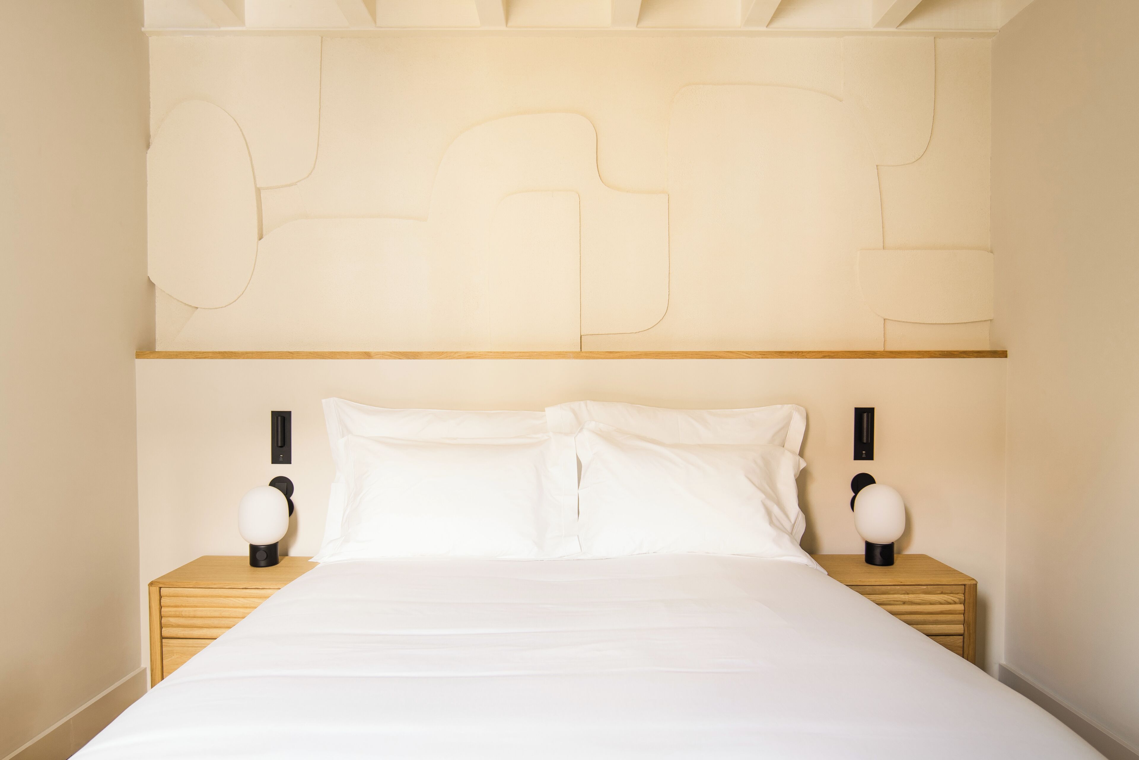 A neatly made bed with white linens, two bedside tables with lamps, and a wall-mounted light fixture.