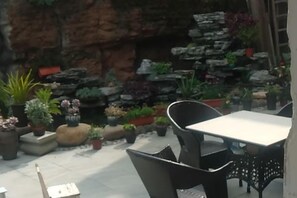 Eine Terrasse im Freien mit Tisch und Stühlen, umgeben von Topfpflanzen und einer Steinmauer.
