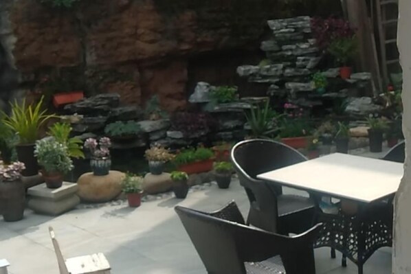 An outdoor patio with a table and chairs, surrounded by potted plants and a rock wall.