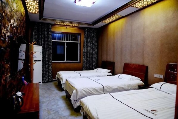 Une chambre d’hôtel avec trois lits, un bureau en bois, une fenêtre avec des rideaux et un luminaire au plafond.