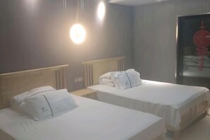 Une chambre d’hôtel avec deux lits, chacun doté de draps et d’oreillers blancs, d’une table de chevet et d’un luminaire fixé au mur.