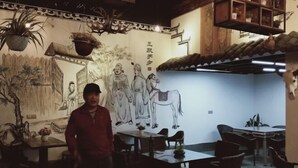 A traditional interior with a mural, tables, chairs, and hanging plants.