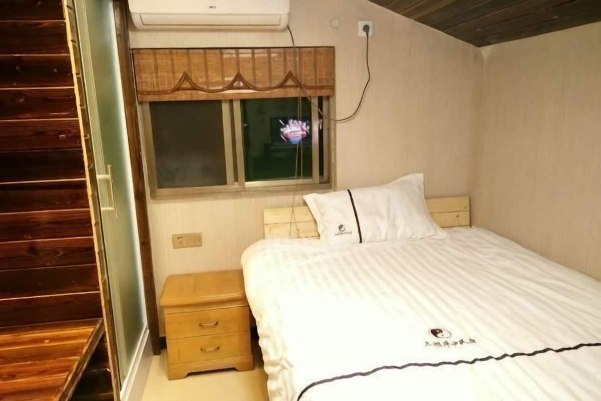 A bedroom with a bed, a bedside table, a window, and a wooden wardrobe.