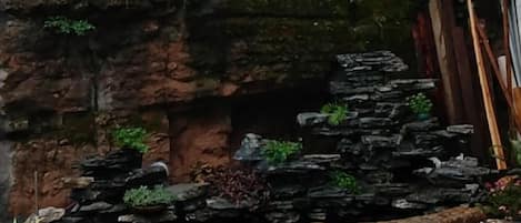 A rock garden with a water feature, surrounded by plants and a wooden fence.