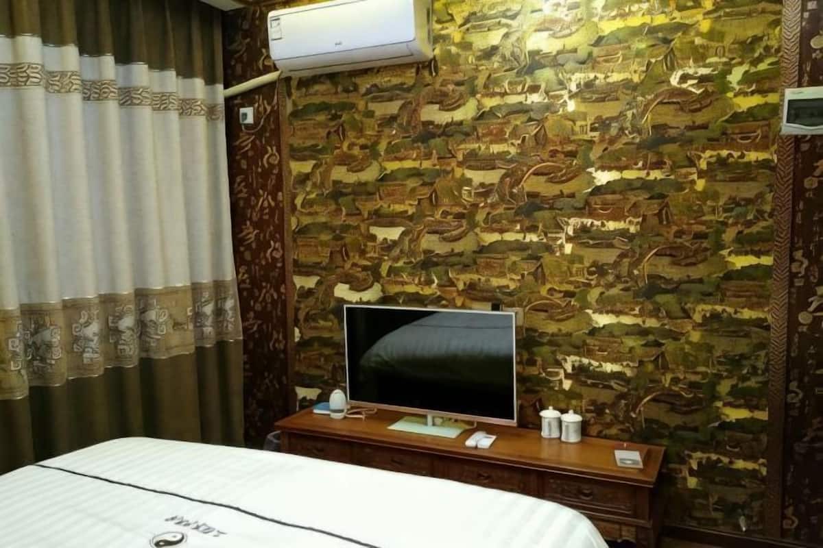 A hotel room with a patterned wallpaper, a flat-screen TV on a wooden dresser, and a bed with a white bedspread.