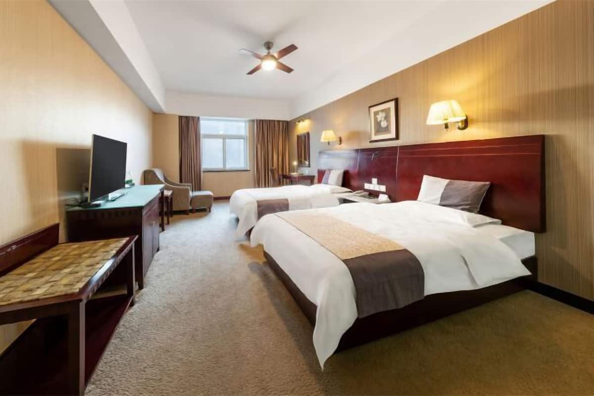 Habitación de hotel con dos camas, un escritorio, una silla, un televisor y un ventilador de techo.