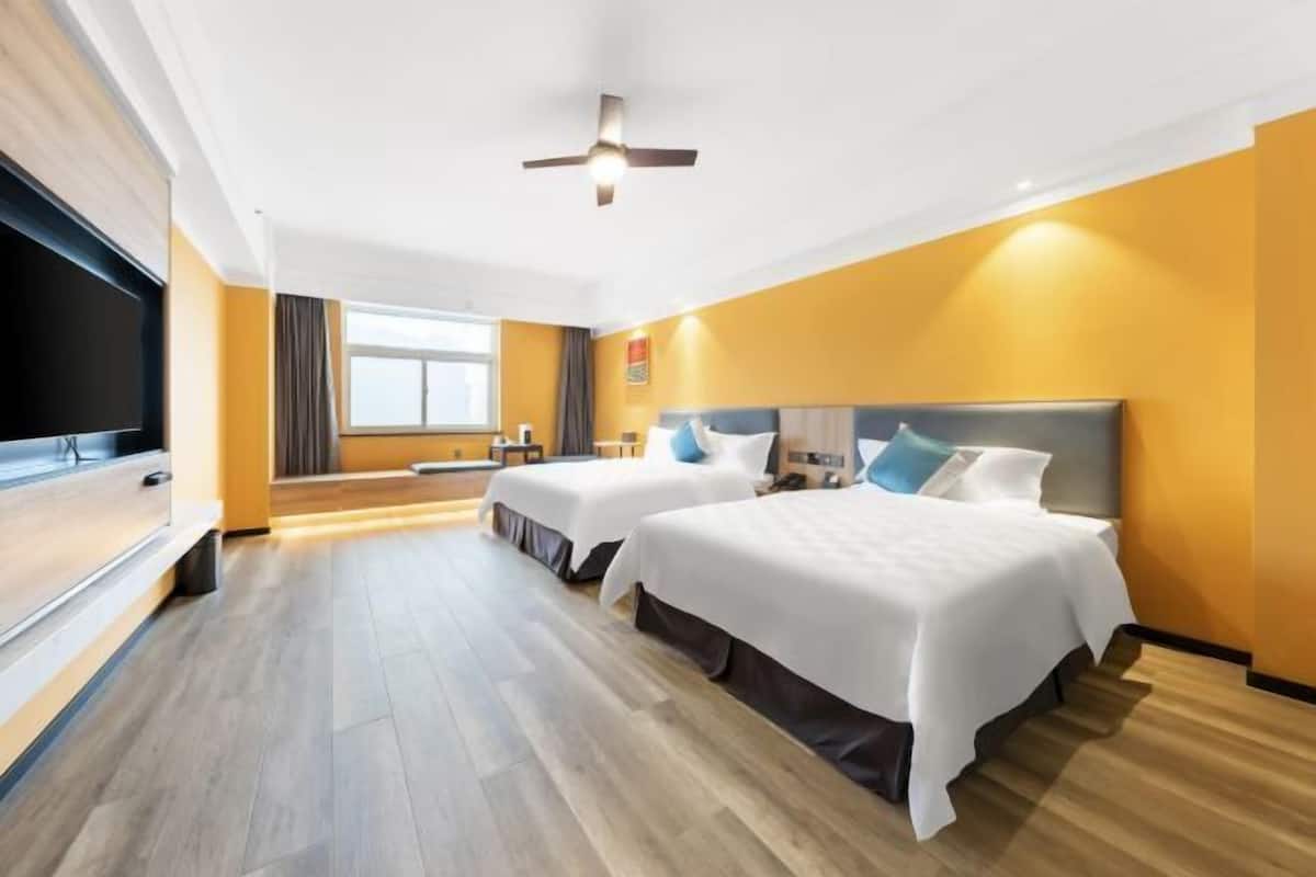 Habitación de hotel con dos camas, televisión, ventilador de techo y ventana con cortinas.