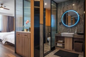 A modern hotel room with a wooden cabinet, a round mirror with a blue light, a bed, and a bathroom with a sink and toilet. - Hai Tian Holiday Inn (Zhengzhou)