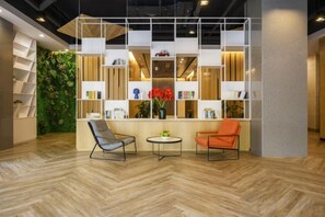 A modern interior with a wooden floor, a seating area with two chairs, a small table, and a bookshelf with various items.