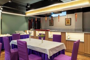 Un espace repas avec des chaises et des tables violettes, un comptoir où est affiché le menu, et un mur orné de tableaux.