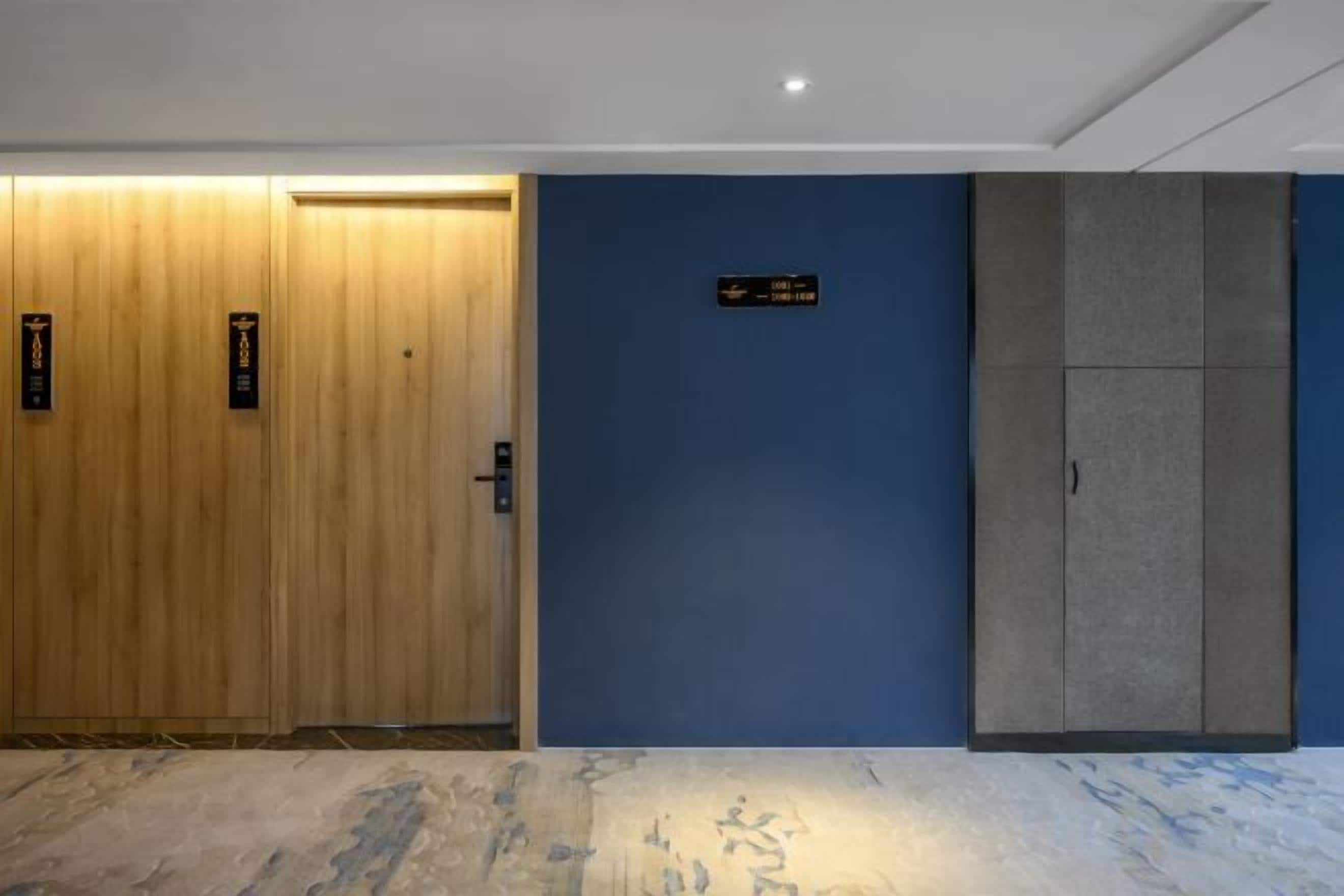 Habitación de hotel con puerta de madera, pared azul y armario gris.