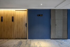A hotel room with a wooden door, a blue wall, and a grey wardrobe. - Hai Tian Holiday Inn (Zhengzhou)