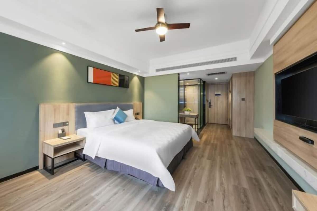 Una habitación de hotel moderna con cama, mesita de noche, televisor y ventilador de techo.