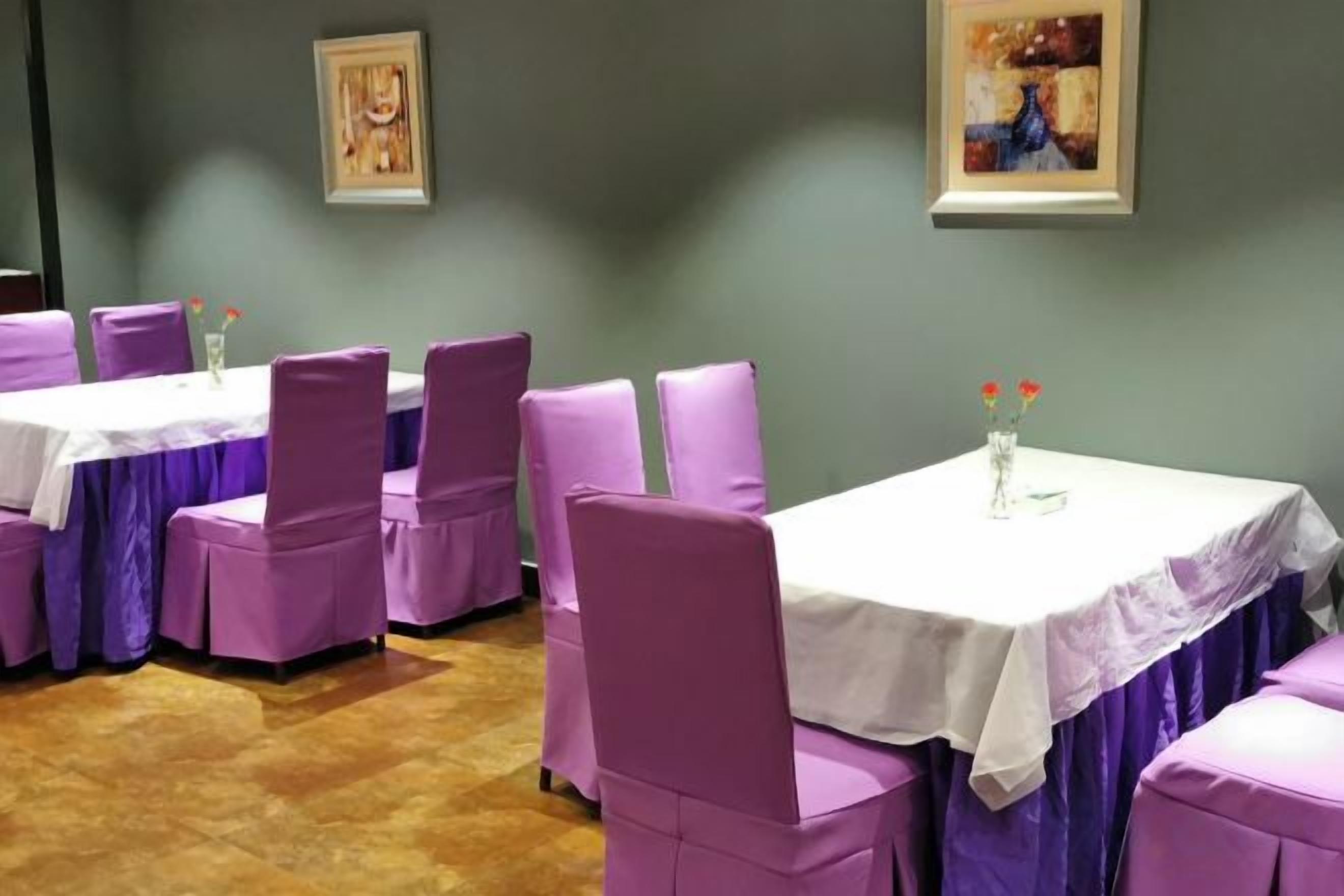 A dining area with tables and chairs, a wooden floor, and artwork on the walls.