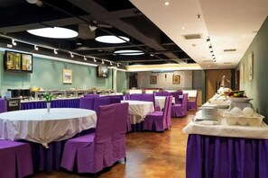 A dining area with round tables and purple chairs, a buffet setup, and a kitchen in the background. - Hai Tian Holiday Inn (Zhengzhou)