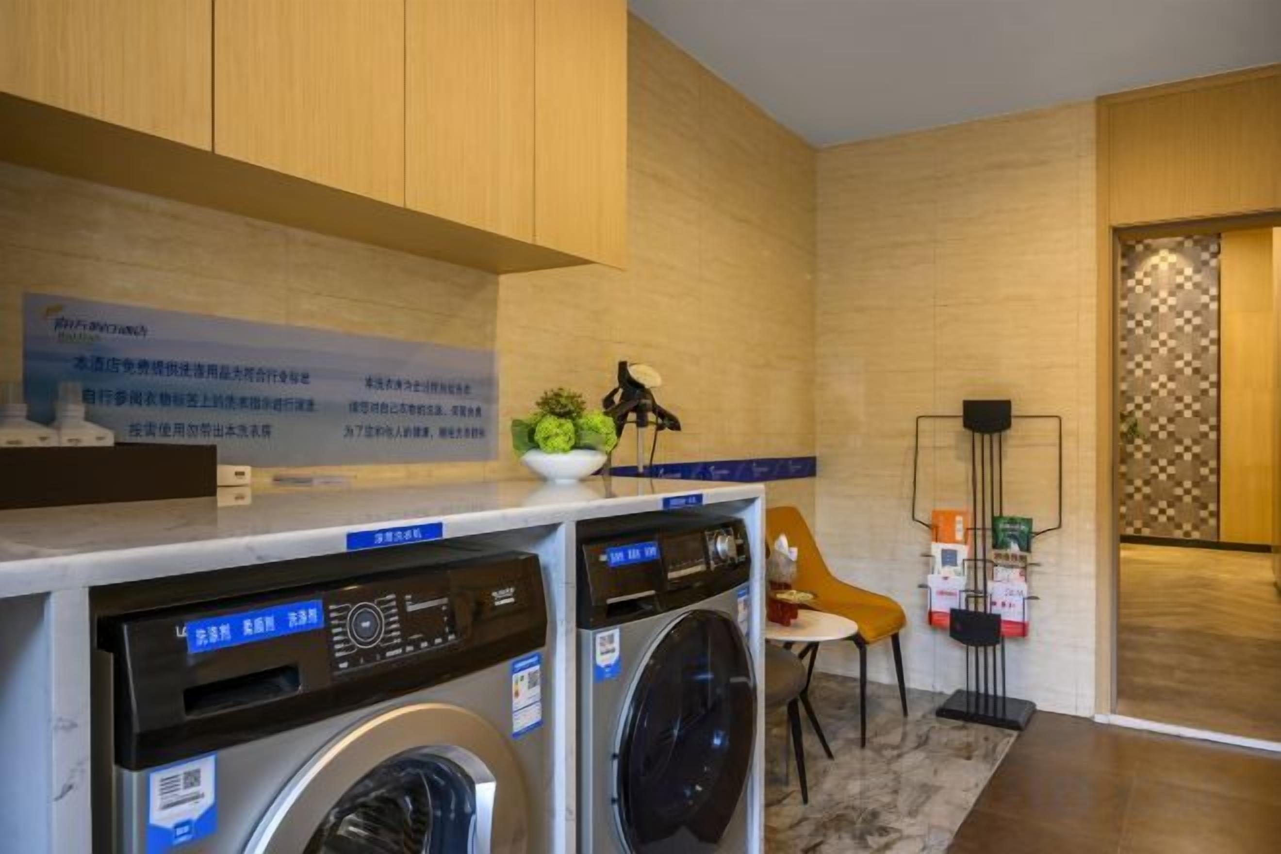 A laundry area with two washing machines, a small table with a plant, and a chair.