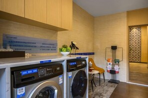 A laundry area with two washing machines, a small table with a plant, and a chair. - Hai Tian Holiday Inn (Zhengzhou)