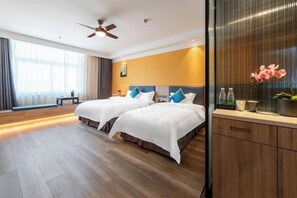 Quarto de hotel com duas camas, um ventilador de teto, uma janela grande com cortinas e piso de madeira.