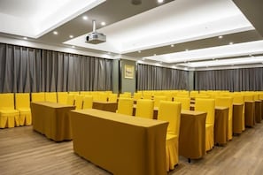 A conference room with rows of yellow chairs and tables, a projector, and a large grey curtain backdrop. - Hai Tian Holiday Inn (Zhengzhou)