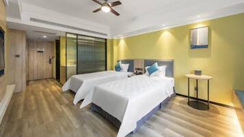 A hotel room with two beds, a ceiling fan, a small table, and a wall-mounted artwork.
