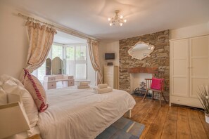 A bedroom with a large bed, a stone wall, a fireplace, a mirror, and a wardrobe.