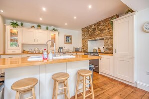 A kitchen with a large island, white cabinets, a stone accent wall, and a clock on the wall.
