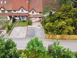 Un immeuble résidentiel avec un toit recouvert de tuiles rouges, une cour avant avec une zone pavée et un grand arbre.