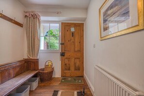 A hallway with a wooden bench, a door, a window, a radiator, and a framed picture on the wall.