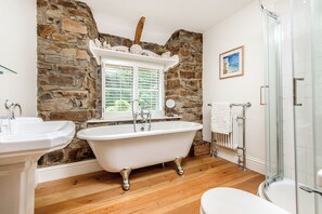 A bathroom with a stone wall, a freestanding bathtub, a white sink, and a glass shower enclosure.
