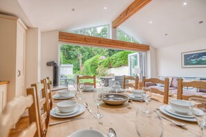 Un coin repas avec une table dressée pour quatre personnes, des chaises en bois et une vue sur un jardin grâce à de grandes fenêtres.
