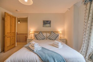 A neatly made bed with towels, a painting on the wall, and a wooden door.