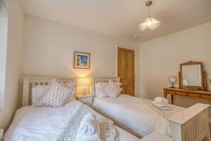 A bedroom with two beds, a wooden door, a bedside table with a lamp, and a mirror.