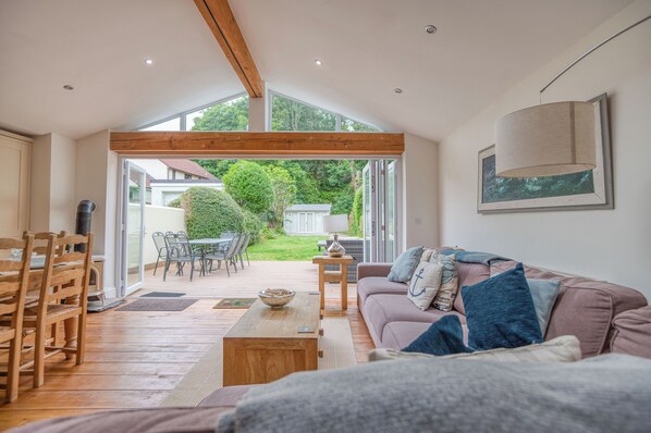 A spacious living area with a wooden ceiling, a sofa, a coffee table, and a dining area with chairs and a table.