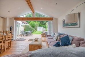 A spacious living area with a wooden ceiling, a sofa, a coffee table, and a dining area with chairs and a table.