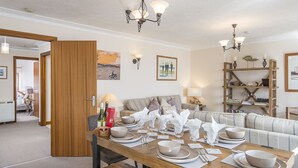 A dining area with a wooden table set for four, a sofa, and a bookshelf.