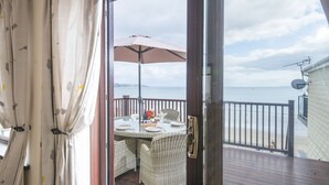 A balcony with a table set for dining, overlooking a beach.