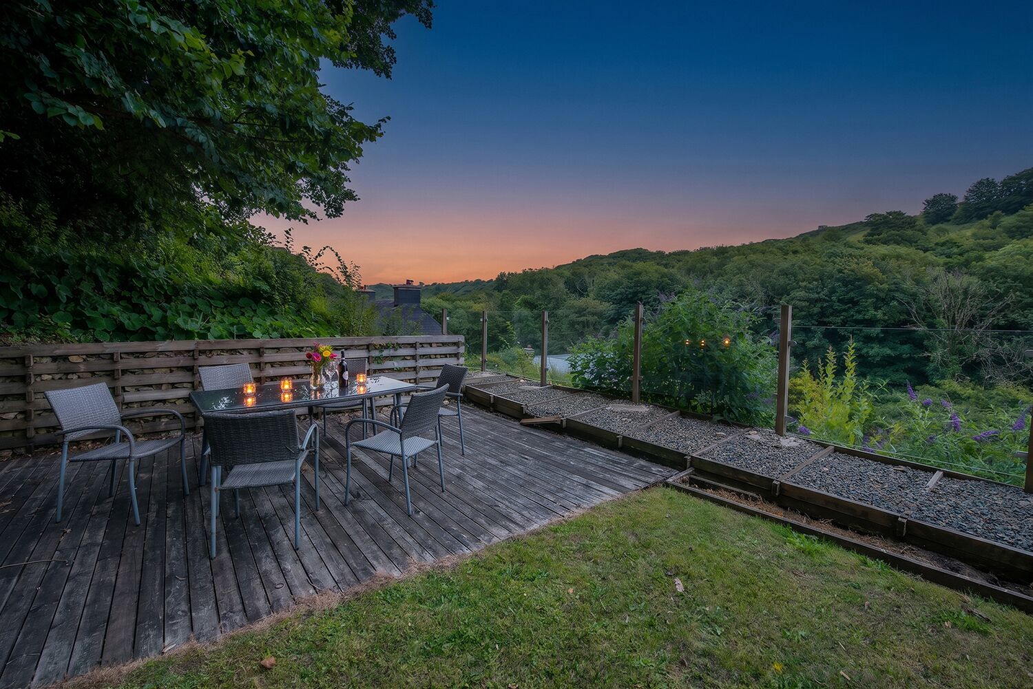 An outdoor deck with a table and chairs, surrounded by greenery and overlooking a hilly landscape.