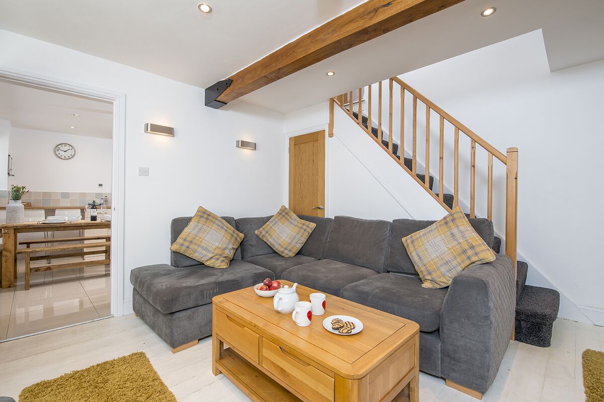 A modern living room with a grey sofa, wooden coffee table, and a staircase with wooden railings.