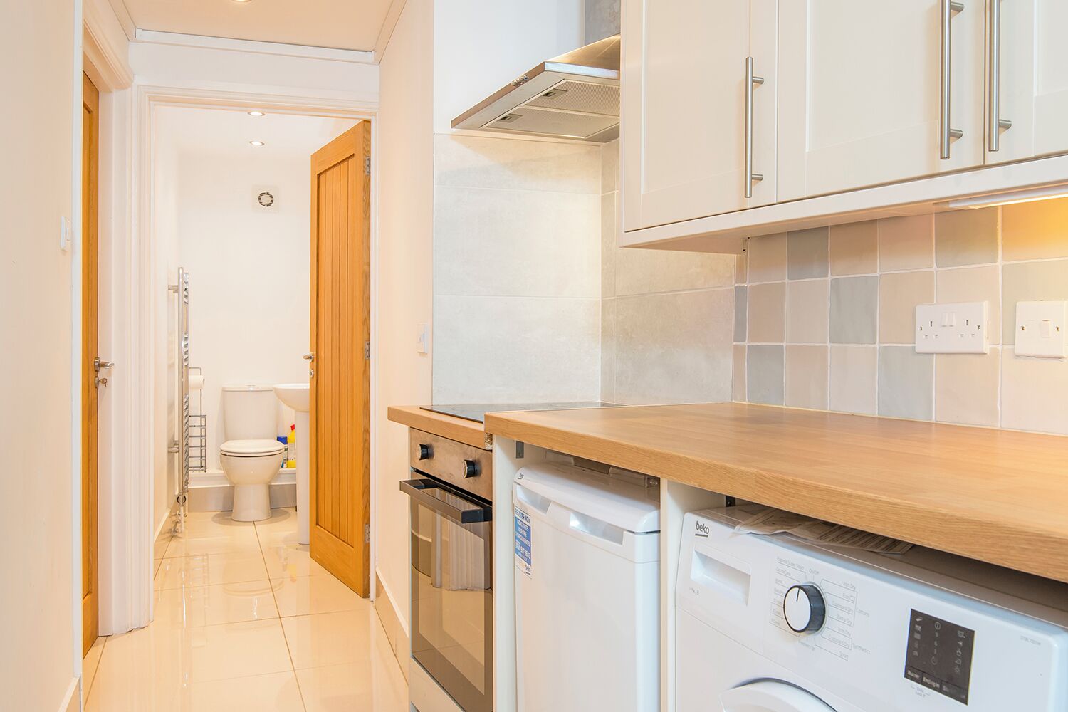 A compact kitchen with a wooden countertop, a washing machine, and a small oven.