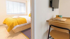 Une chambre avec un lit, un téléviseur fixé au mur et une petite table sur laquelle se trouve une assiette de nourriture.