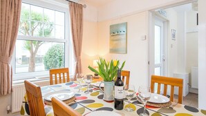 A dining area with a table set for two, a bottle of wine, and a vase with green plants. - 8 Garn Ingli, Holiday Home Fishguard, Sleeps 5, 3 bedrooms,  bathrooms (Fishguard)