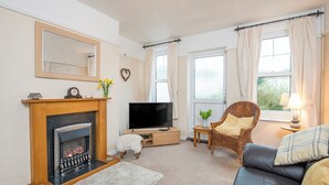 A living room with a fireplace, television, sofa, and a window with curtains. - 8 Garn Ingli, Holiday Home Fishguard, Sleeps 5, 3 bedrooms,  bathrooms (Fishguard)