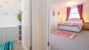 A bedroom with a bed, a window with curtains, a bedside table, and a wall-mounted lamp. - 8 Garn Ingli, Holiday Home Fishguard, Sleeps 5, 3 bedrooms,  bathrooms (Fishguard)