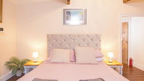 A bedroom with a large bed, two bedside tables with lamps, a framed picture on the wall, and a door to the right. - 90 Main Street, Holiday Cottage Pembroke, Sleeps 4, 2 bedrooms,  bathrooms (Pembroke)